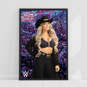 Può includere: Una donna vestita con un completo nero con un cappello da cowboy, un top nero e una cintura nera con una fibbia dorata. È in piedi di fronte a una folla di persone. Il testo "Trish Stratus" è scritto in lettere rosa su uno sfondo viola.