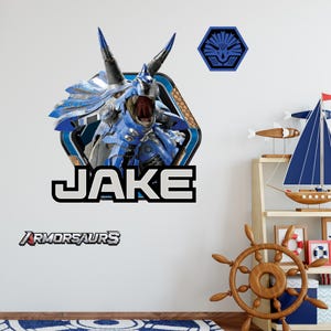 May include: A wall decal featuring a blue and silver armored dinosaur with the name "JAKE" in bold white letters. The decal also includes the word "ARMORSAURS" in a stylized font. A blue and black hexagon emblem is also present.