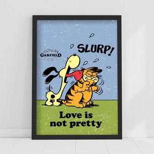 May include: A framed vintage Garfield poster. The poster features Garfield being licked by a dog, with the word "SLURP!" above them. The text "Love is not pretty" is at the bottom. The poster has a blue and green background.