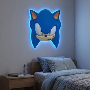 May include: A blue Sonic the Hedgehog wall light fixture with a neon blue outline. The light is mounted on a gray wall above a bed with blue bedding. The nightstand has a book and water bottle.