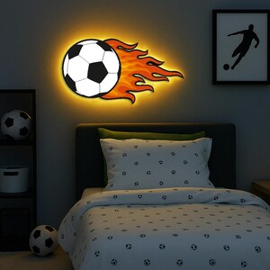 May include: A wall decoration featuring a soccer ball with flames. The black and white soccer ball is set against orange and red flames, with a warm yellow glow. A framed silhouette of a soccer player is also visible on the wall.
