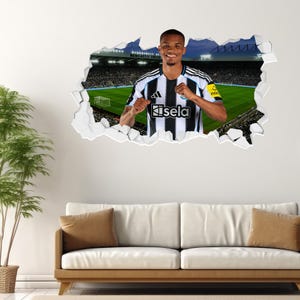 May include: A wall decal featuring a soccer player in a black and white striped jersey, emerging from a torn wall. The background shows a stadium with a green field and spectators. The player is smiling and has his fists clenched.