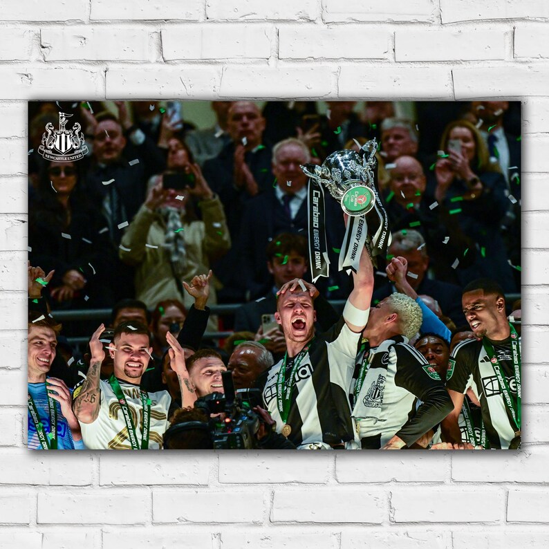 May include: A group of people celebrating with confetti and a silver trophy. The trophy has a green and white ribbon that says "Carabao Energy Cup Final". The people are wearing black and white uniforms and are holding the trophy up in the air.