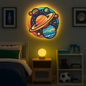 May include: A vibrant, illuminated wall decoration depicting planets and stars in a cartoon style. The circular artwork has a bright yellow border and is mounted above a bed. A small, spherical lamp rests on a wooden bedside table in a child's room.