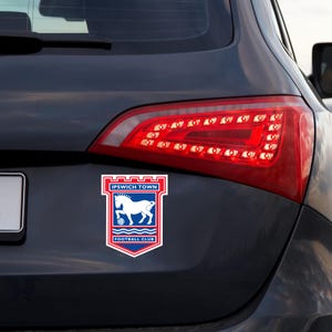 May include: A white and blue car sticker with the Ipswich Town Football Club logo. The logo features a white horse with a red and blue shield and the words "Ipswich Town Football Club".