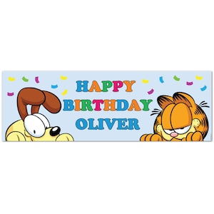 May include: A light blue banner featuring the text "HAPPY BIRTHDAY OLIVER" in colourful letters. Cartoon images of a dog and Garfield the cat flank the text, with confetti scattered around the design.
