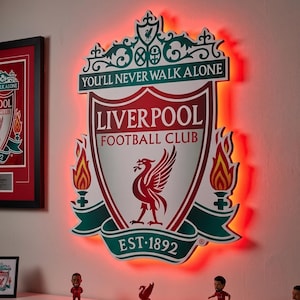Può includere: Un'insegna da parete con lo stemma del Liverpool Football Club in rosso, bianco e verde, con il testo YOU'LL NEVER WALK ALONE, LIVERPOOL FOOTBALL CLUB ed EST 1892. L'insegna è retroilluminata da una vivace luce LED di colore rosso.