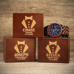 May include: Three wooden boxes with engraved tuxedo designs and personalized names. The boxes are labeled "Chase Groom 12.10.2026", "Joseph Groomsman 12.10.2026", and "Steven Best Man 12.10.2026".