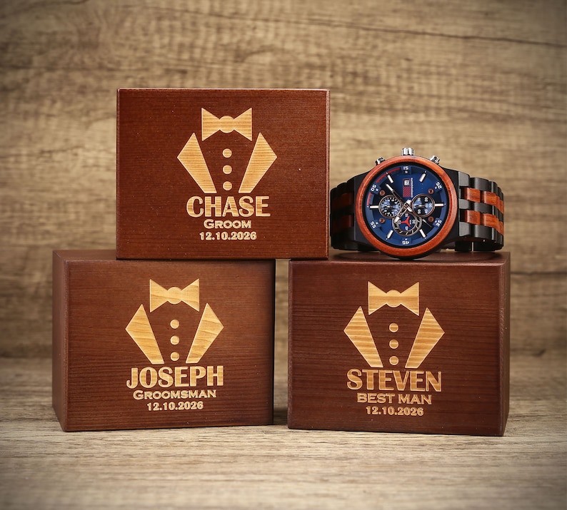 May include: Three wooden boxes with engraved tuxedo designs and personalized names. The boxes are labeled "Chase Groom 12.10.2026", "Joseph Groomsman 12.10.2026", and "Steven Best Man 12.10.2026".