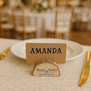 May include: A place setting featuring a kraft paper name card with "AMANDA" in black letters. The card is held by a wooden log slice base. The base is engraved with "Marcia Reuben" and the date "November 18, 2027".