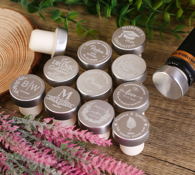 May include: A set of 12 silver bottle stoppers with various engraved designs. The designs include names, dates, and phrases like "Eat Drink and Be Merry", "Cheers", "Love", and "Our Forever Begins Now".