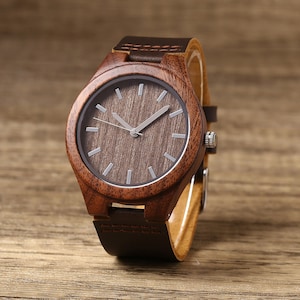 Op de afbeelding: Een bruin houten polshorloge met een bruin leren bandje. De wijzerplaat van het horloge is rond en heeft een donkerbruin houtnerfpatroon.
