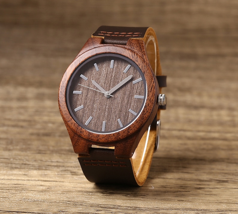 Op de afbeelding: Een bruin houten polshorloge met een bruin leren bandje. De wijzerplaat van het horloge is rond en heeft een donkerbruin houtnerfpatroon.