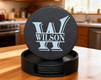 May include: A set of black coasters with a holder, featuring a light blue monogram design with the name "WILSON". The coasters are round and made of a textured material. The holder is also black and holds multiple coasters.