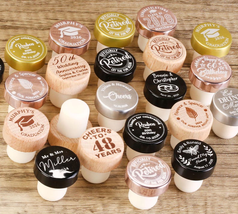 May include: Assortment of personalized bottle stoppers with various designs and text, including graduation, wedding anniversary, birthday, and retirement. The stoppers are made of wood, metal, and cork.