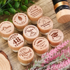 May include: A collection of ten wooden bottle stoppers with personalized engravings. The stoppers feature various designs and messages, including "Cheers to 48 Years", "Officially Retired", "Happy Retirement Martin", "Murphy's Graduation 2026", "Thanks for Celebrating Reuben", "Aged to Perfection Bennett's 55th Birthday", "Florence & Spencer Our Forever Begins Now", "Vivian & Howard Cheers", and "50th Wedding Anniversary Sophia & Carlos".