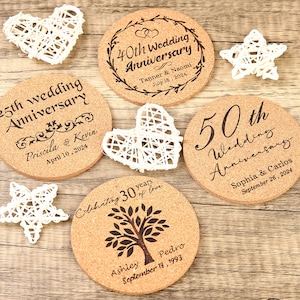 May include: Set of five round cork coasters with personalised wedding anniversary messages. The coasters feature different designs, including a heart, a tree, and a star. The text on the coasters includes the couple's names, the anniversary year, and the date.