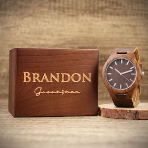 Op de afbeelding: Een houten horloge met een bruin leren bandje in een houten doos. De doos is gegraveerd met de naam "BRANDON" en het woord "Groomsman".