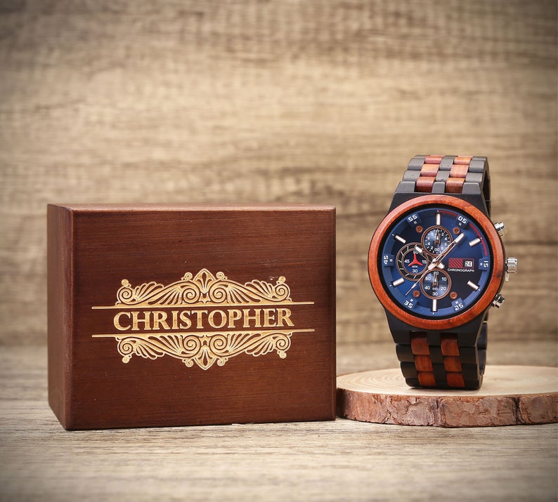 May include: A wooden watch with a blue face and black and red accents. The watch is in a wooden box with the name "CHRISTOPHER" engraved on the top.