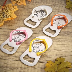 Pode incluir: Quatro abridores de garrafas prateados em forma de chinelos, cada um com uma correia de cor diferente: branco, laranja, rosa e amarelo. Cada abridor tem um design único com nomes e datas, ideal para lembranças de casamento.