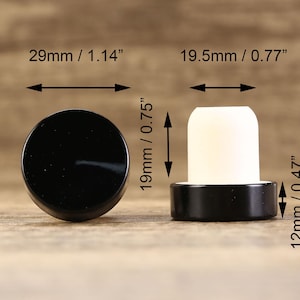 May include: Two black bottle stoppers with a white cork insert. The larger stopper measures 1.14 inches in diameter and 0.75 inches in height. The smaller stopper measures 0.77 inches in diameter and 0.47 inches in height.