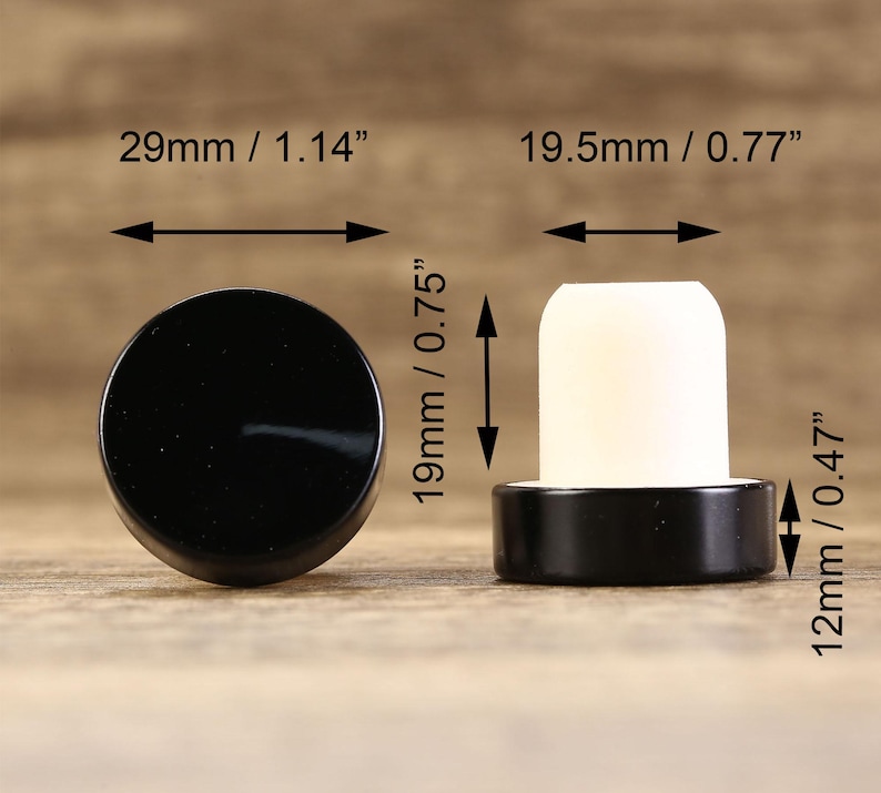 May include: Two black bottle stoppers with a white cork insert. The larger stopper measures 1.14 inches in diameter and 0.75 inches in height. The smaller stopper measures 0.77 inches in diameter and 0.47 inches in height.