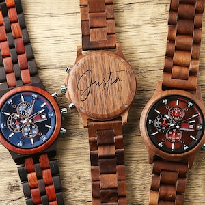 May include: Three wooden wristwatches with chronograph faces. The watch on the left has a blue face with red accents. The watch in the middle has a wooden face with the name "Justin" engraved on it. The watch on the right has a red face with black accents.