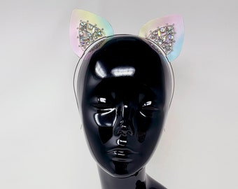 May include: A black mannequin head wearing a headband with iridescent cat ears. The ears are decorated with rhinestones.