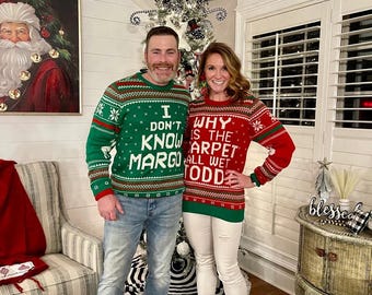 Può includere: Una coppia indossa maglioni di Natale abbinati con frasi divertenti. Il maglione dell'uomo dice "Non lo so Margo" e il maglione della donna dice "Perché il tappeto è tutto bagnato Todd".