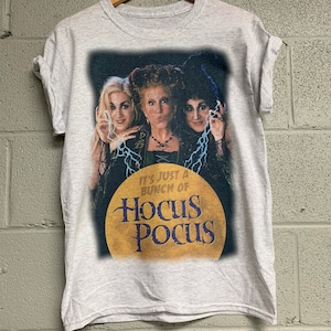 May include: A gray t-shirt with a graphic print of the three Sanderson sisters from the movie "Hocus Pocus". The text "It's just a bunch of Hocus Pocus" is printed on the shirt.
