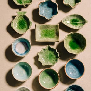 May include: An assortment of ceramic serving dishes in various shapes and shades of green and blue. The collection includes leaf-shaped, fish-shaped, and round bowls, as well as a rectangular dish. The text "CHEF'S TABLEWARE" is visible.