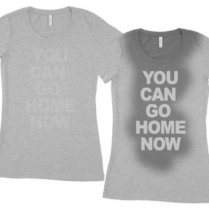 May include: Two gray t-shirts with the text "You can go home now" printed on them. The text on the left shirt is faded, while the text on the right shirt is clear.