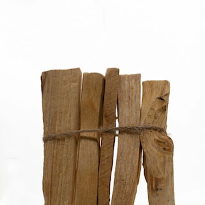 Può includere: Un fascio di bastoncini di palo santo marroni legati insieme con uno spago. I bastoncini sono disposti a zig zag.