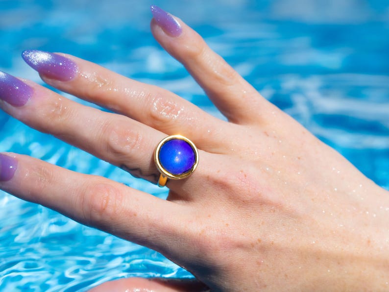 Small gold circle mood ring worn on hand in water from swimming pool, long purple nails on hand