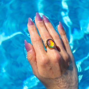 Small oval shape gold waterproof mood ring worn on hand in water from a swimming pool