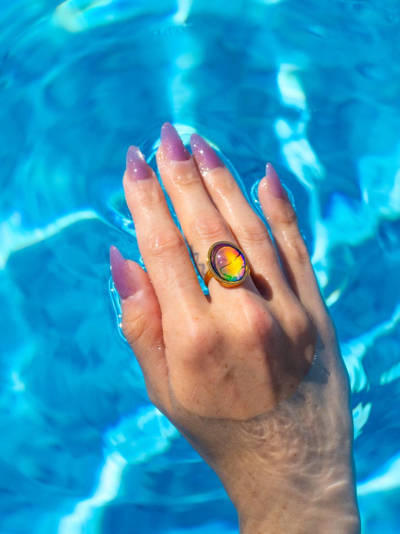 Small oval shape gold waterproof mood ring worn on hand in water from a swimming pool