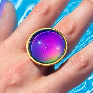 Large gold circle mood ring with purple stone, cover photo, worn on hand in water in swimming pool. Cropped for google shopping cover photo.