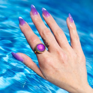 Small gold circle mood ring worn on hand in water from swimming pool, long purple nails on hand