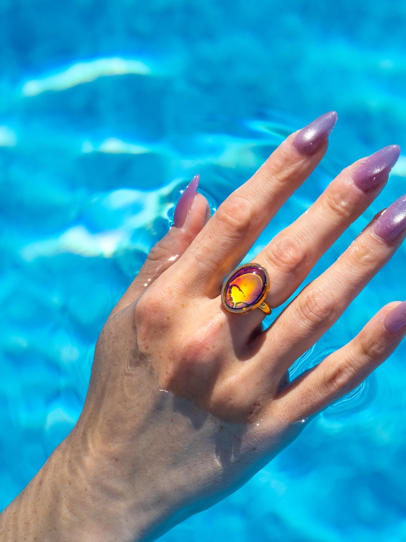 Small oval shape gold waterproof mood ring worn on hand in water from a swimming pool