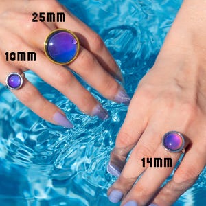 Round mood rings of three sizes small medium and large on hands in swimming pool, gold and silver rings in blue and purple tones