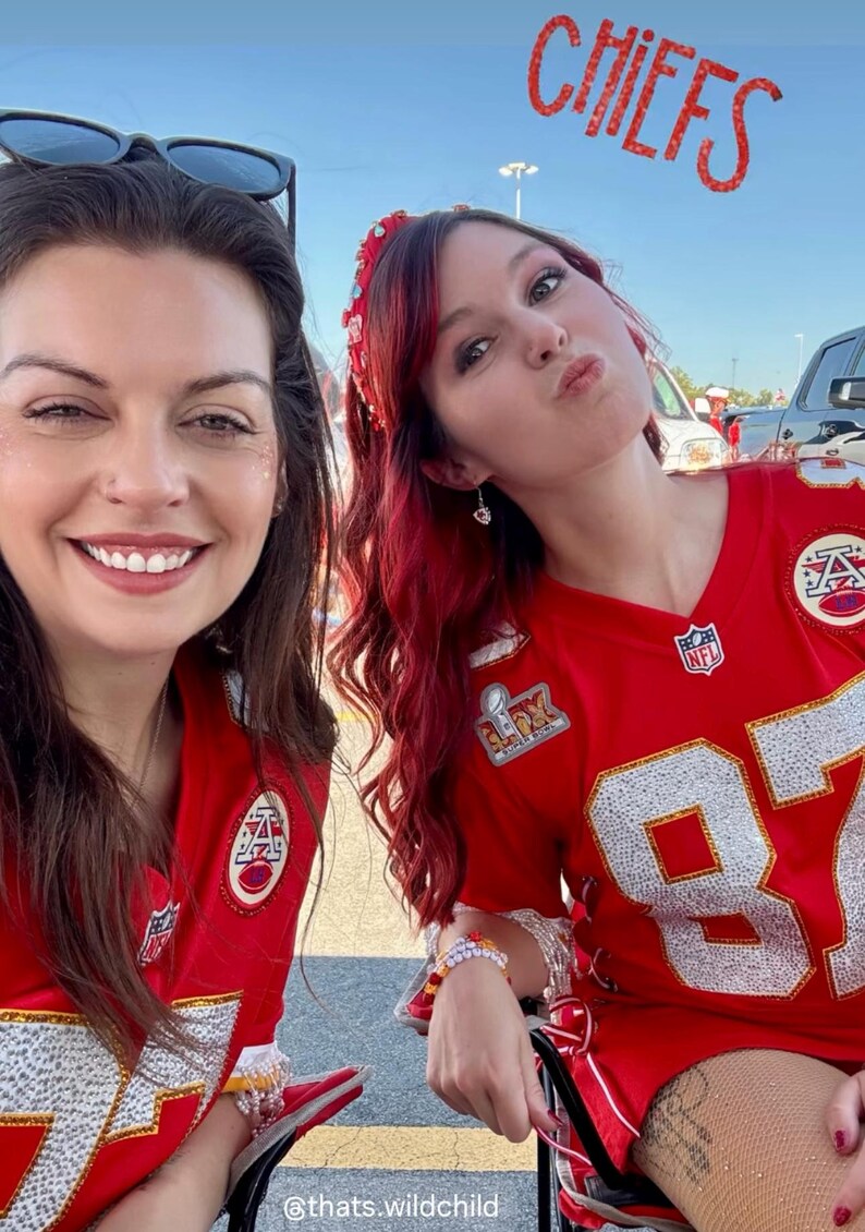 Puede incluir: Dos mujeres con camisetas de f&uacute;tbol rojas y blancas. Las camisetas tienen el n&uacute;mero 87. La palabra "CHIEFS" es visible en el fondo. Una mujer tiene el pelo rojo y una diadema. La otra mujer est&aacute; sonriendo.