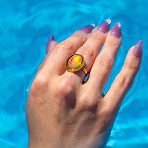 Small oval shape gold waterproof mood ring worn on hand in water from a swimming pool