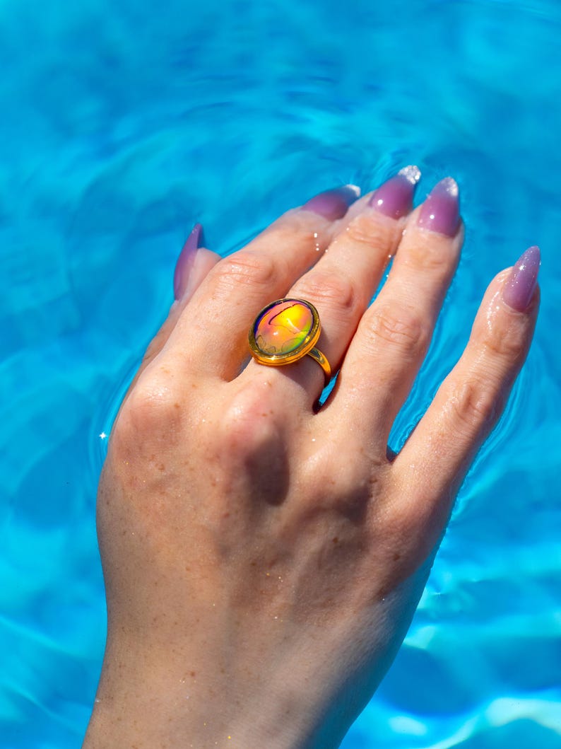 Small oval shape gold waterproof mood ring worn on hand in water from a swimming pool