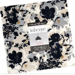 May include: A square fabric swatch with a floral pattern in black, gray, and gold on a cream background. The fabric is labeled "Arabesque" by Moda Fabrics & Supplies.