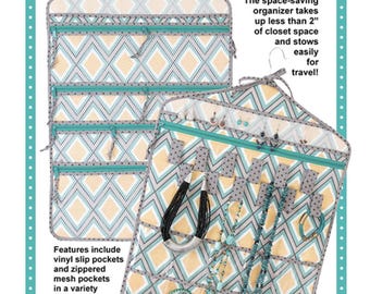 May include: Double-sided hanging organizer with a geometric pattern in yellow, gray, and teal. The organizer features vinyl slip pockets, zippered mesh pockets, and bars for earrings. Text reads "BLING IT ON!" and "ByAnnie's Soft and Stable™ makes it sturdy!"