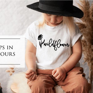 May include: A white t-shirt with a black graphic of a wildflower and the word "wildflower" in black script.