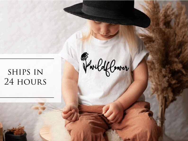 May include: A white t-shirt with a black graphic of a wildflower and the word "wildflower" in black script.