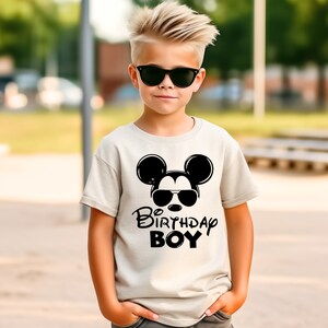 May include: A white t-shirt with a black Mickey Mouse graphic wearing sunglasses and the text "Be Birthday Boy".