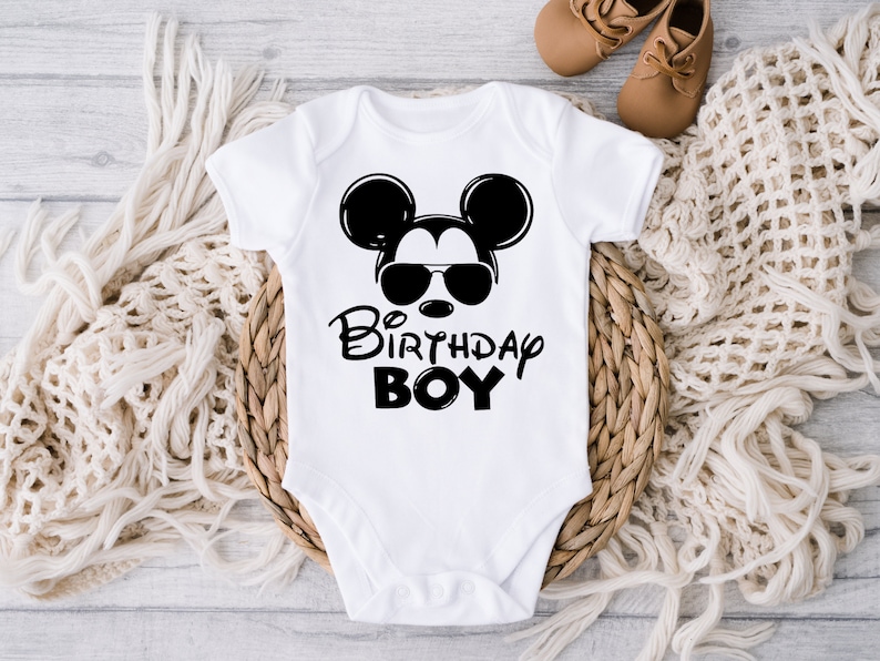 May include: White baby onesie with a black and white illustration of Mickey Mouse wearing sunglasses. The text "Birthday Boy" is printed below the illustration.