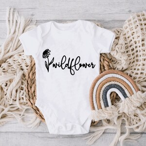 May include: White baby onesie with a black daisy and the text "wildflower" printed on the front.